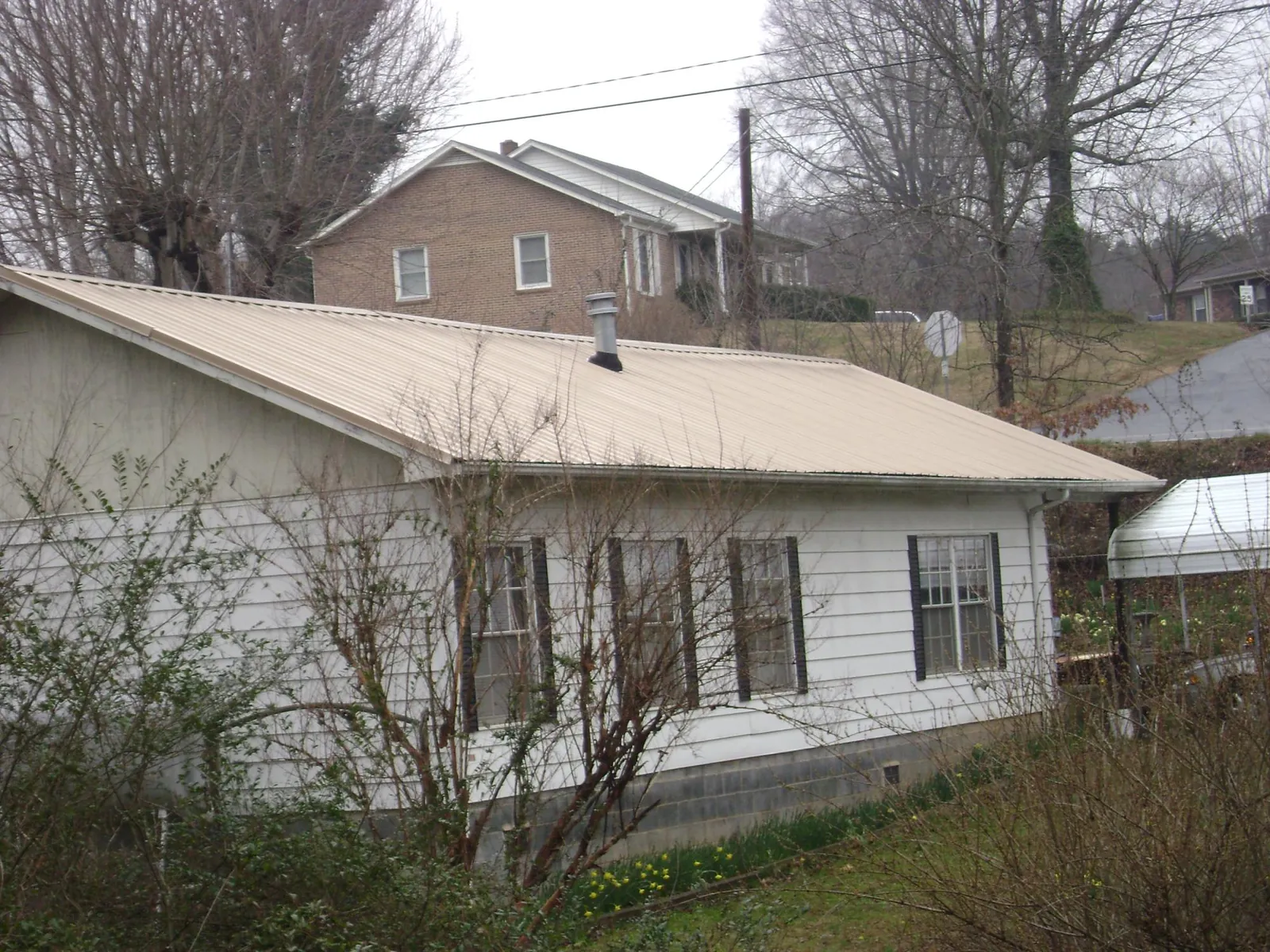 Tan metal roof on a white sided house set into a hillside — Commercial Roofing by Roofing Brothers in Medford